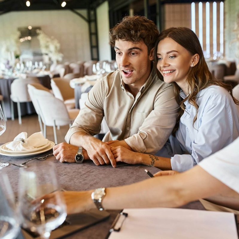 amazed-and-happy-couple-looking-at-laptop-near-event-organizer-at-festive-table-bridal-preparation.jpg